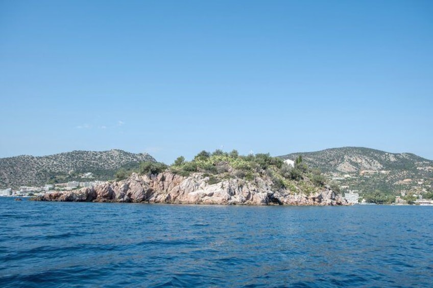 A coastal landscape with rocky cliffs, clear blue water, and distant hills. 2