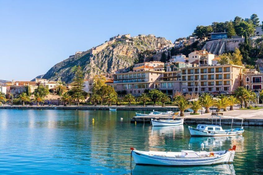 A coastal town with boats docked, a mountain in the background, and buildings along the waterfront. 1