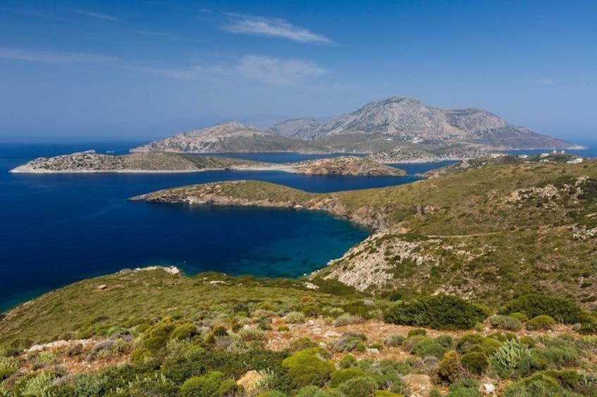 A coastal landscape with a mountain, clear blue sea, and sparse vegetation. 4