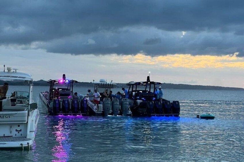 A boat with people boarding, a docked boat in the background, and a sunset over the water. 3