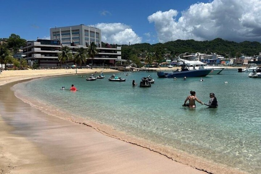 A beach with clear water, boats, and a building in the background. 5