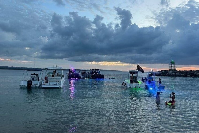 A marina with boats docked, some with colorful lights, and a lighthouse in the background. 2