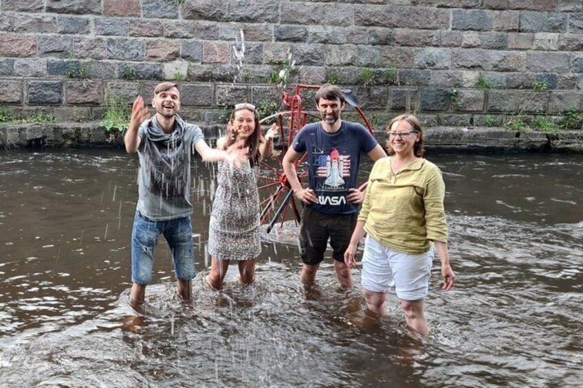 Four people standing in a shallow water body with a stone wall in the background. 1
