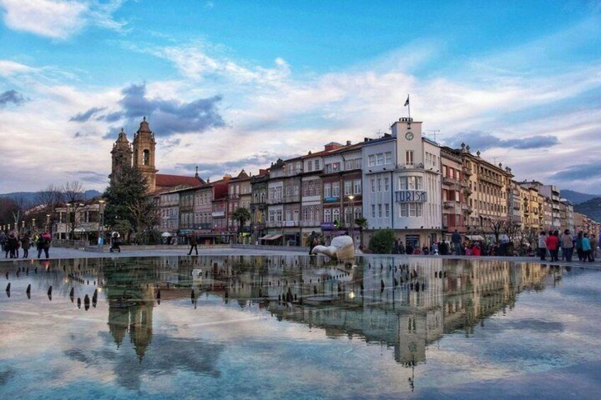 A historic square with a central fountain, buildings, and a church tower. 1