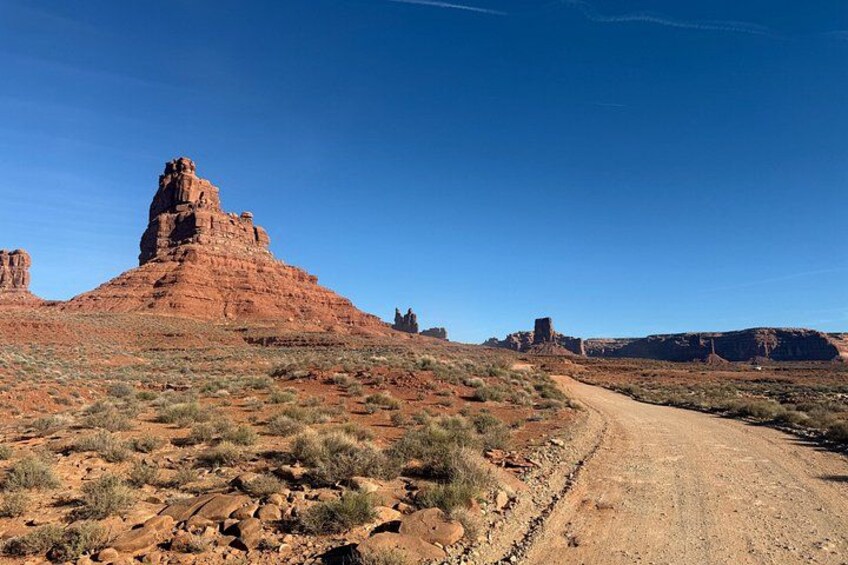 A desert landscape with a prominent red rock formation, a dirt road, and sparse vegetation. 3
