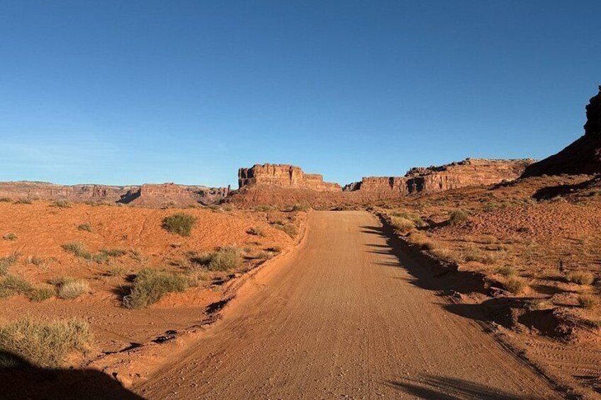 A dirt road in a desert landscape with red rock formations and sparse vegetation. 4