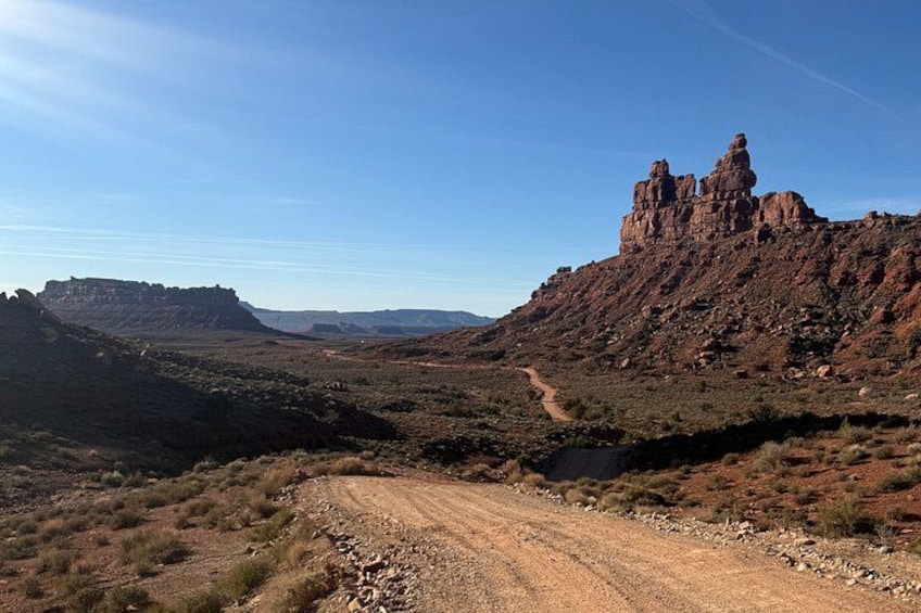 A desert landscape with a dirt road, rocky terrain, and a prominent rock formation. 1
