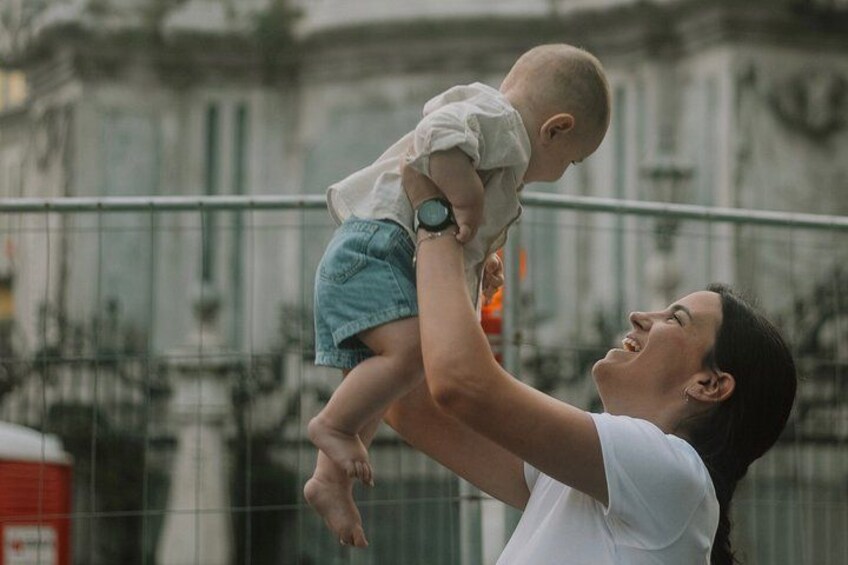 A person holding a child in an urban setting with historical architecture in the background. 2