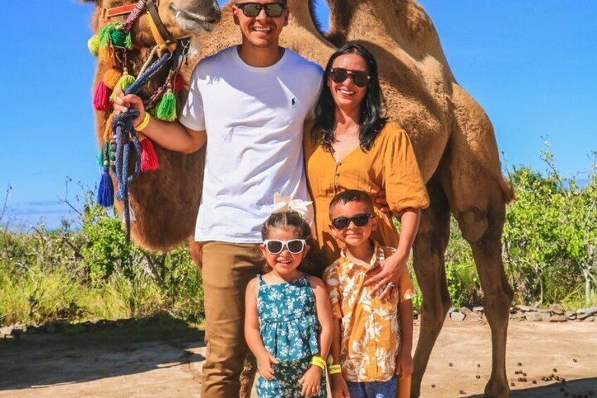 A family with a camel, desert vegetation, and a clear sky. 4