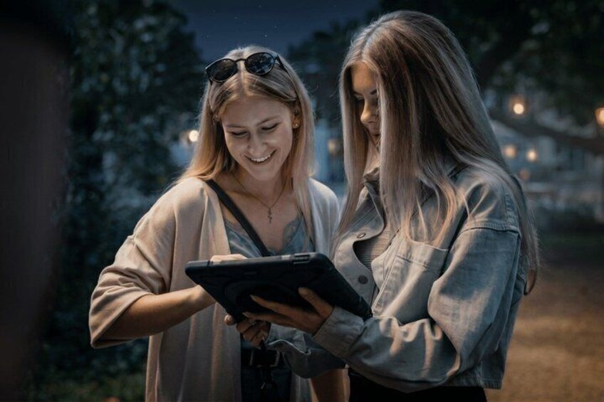 Two people standing outdoors at night, one holding a tablet. 5