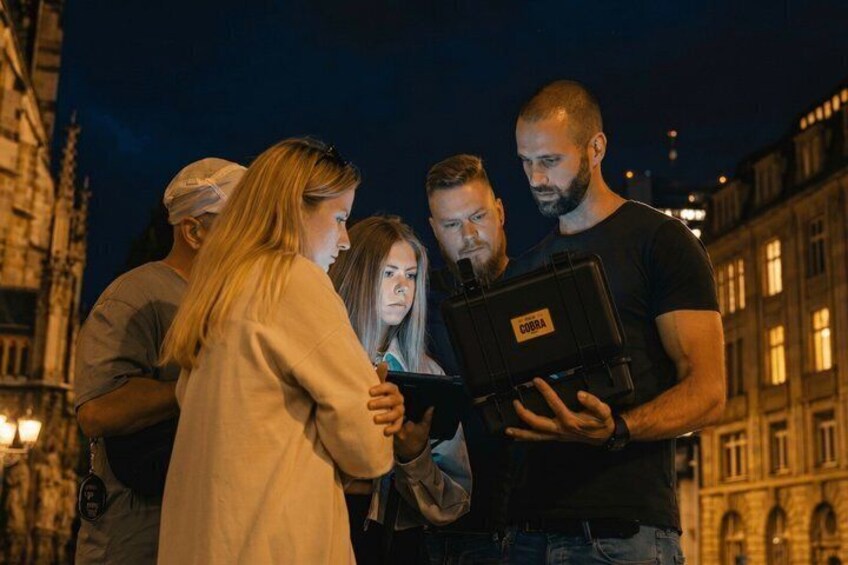 A group of people standing outdoors at night, with a building in the background. 1
