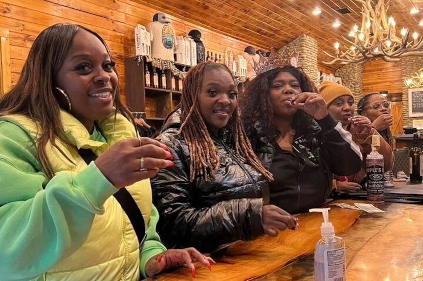 A group of people sitting at a wooden bar with bottles and a chandelier in the background. 3