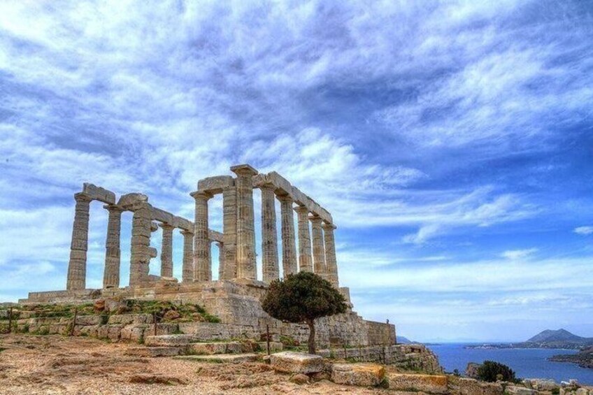 Ancient ruins with columns, a tree, and a coastal landscape. 3