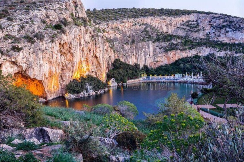 A rocky cliff, a calm lake, and a small building with a roof. 5