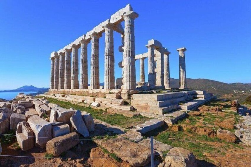 Ancient ruins with columns and stone blocks, set against a clear blue sky and a hilly landscape. 2