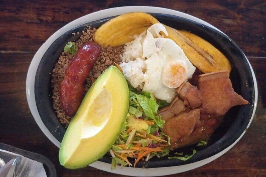 A plate of food with various items including a slice of avocado, a fried egg, a sausage, a piece of meat, a banana, and a salad. 5