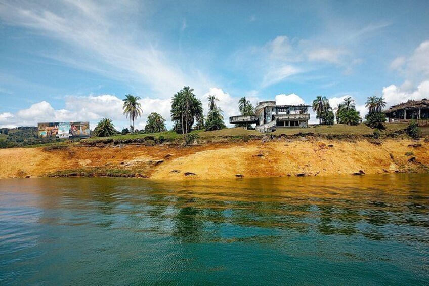 A coastal landscape with a sandy beach, calm water, palm trees, and buildings. 3