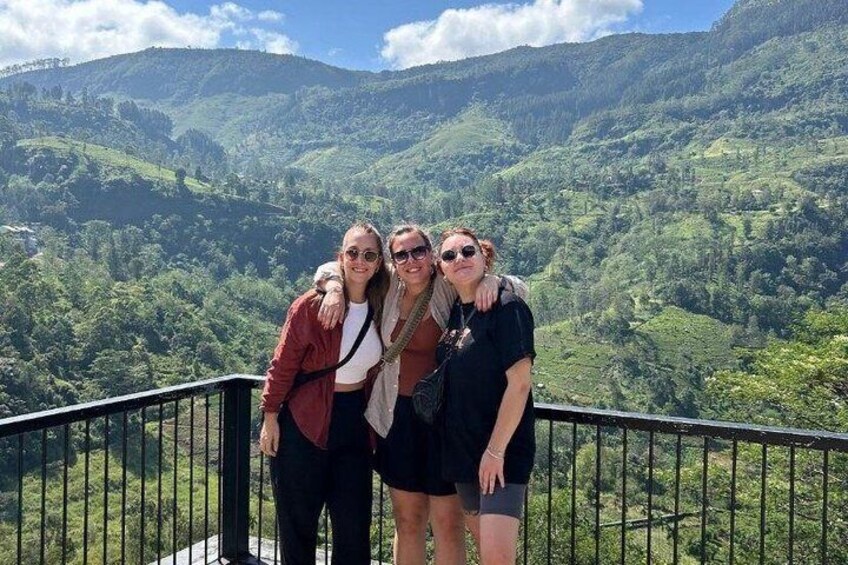 Three people standing on a balcony with a mountainous landscape in the background. 5