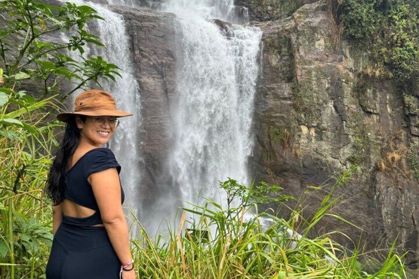 A waterfall with lush greenery and a person in a hat. 4