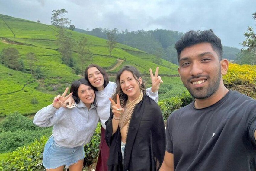 A group of people posing in a hilly, green landscape with tea plantations. 1