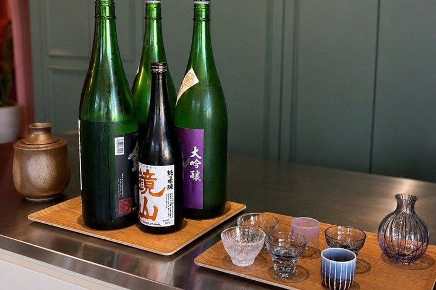 Three green bottles on a wooden tray, a small vase, and various glassware on a kitchen counter. 5