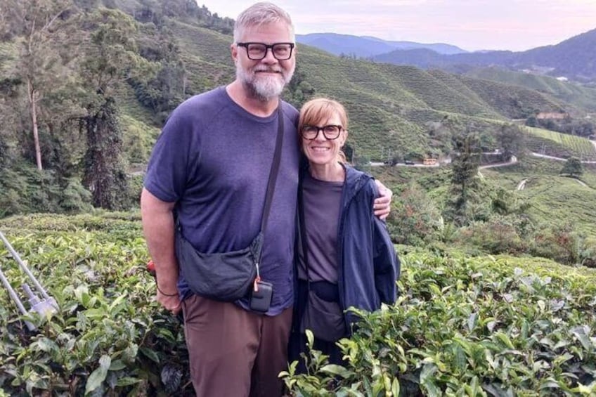 Two people standing on a hillside with tea plantations in the background. 5