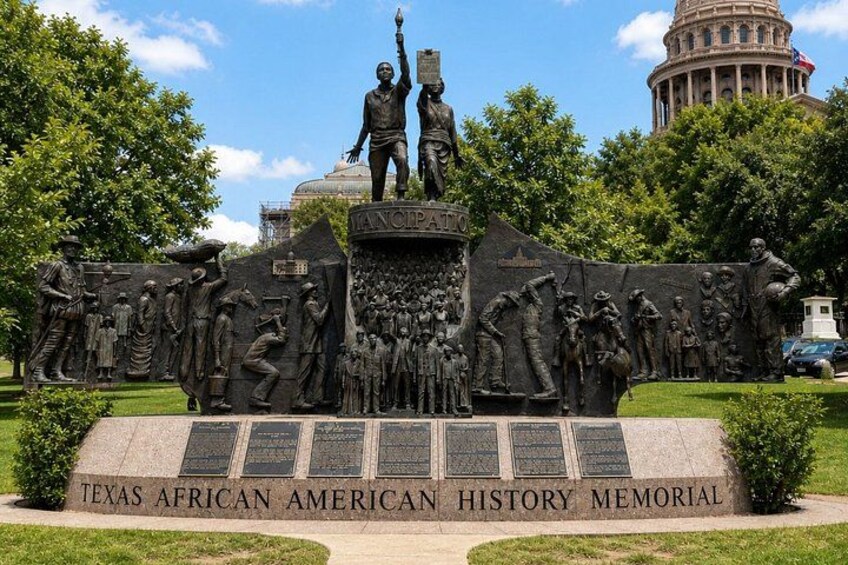 A Texas African American History Memorial with a central statue, inscriptions, and a surrounding relief sculpture. 3