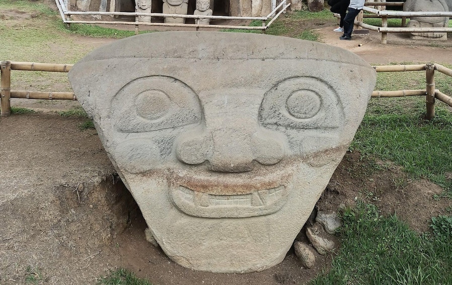 A large stone sculpture with a face, surrounded by a bamboo fence. 1