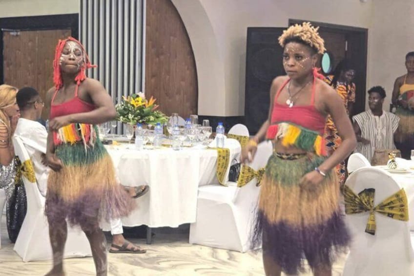 Two individuals in colorful traditional attire dancing at a formal event with tables and guests in the background. 2