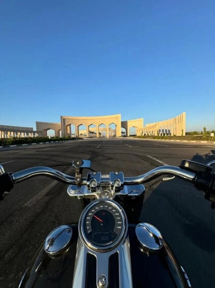 A motorcycle's dashboard and a large, modern building with arches in the background. 4