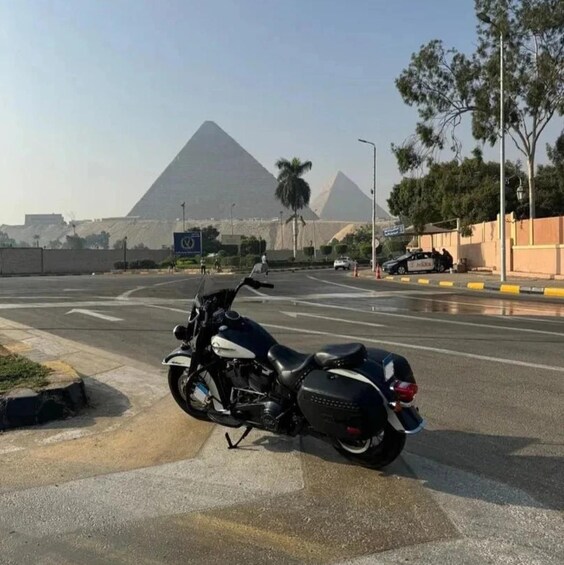 A motorcycle parked on a road with a pyramid in the background. 1