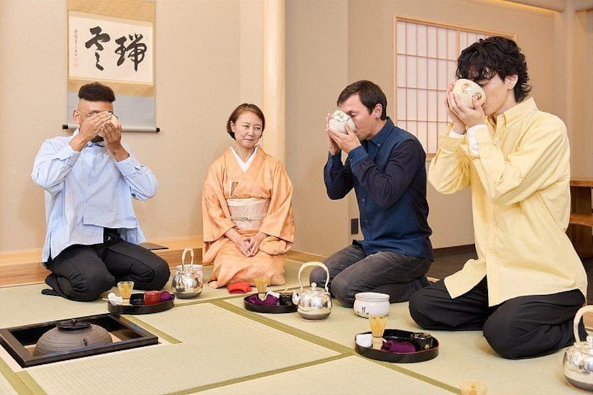 Four people sitting on tatami mats in a traditional Japanese room with tea sets. 1
