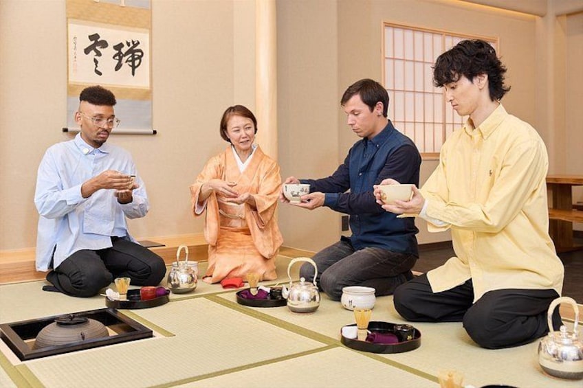 Four people sitting on tatami mats in a traditional Japanese room with tea sets. 4