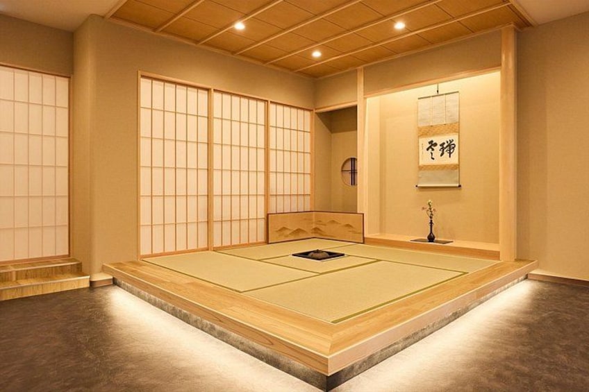 A tatami mat room with sliding doors, a tatami mat in the center, and a hanging scroll with calligraphy. 3