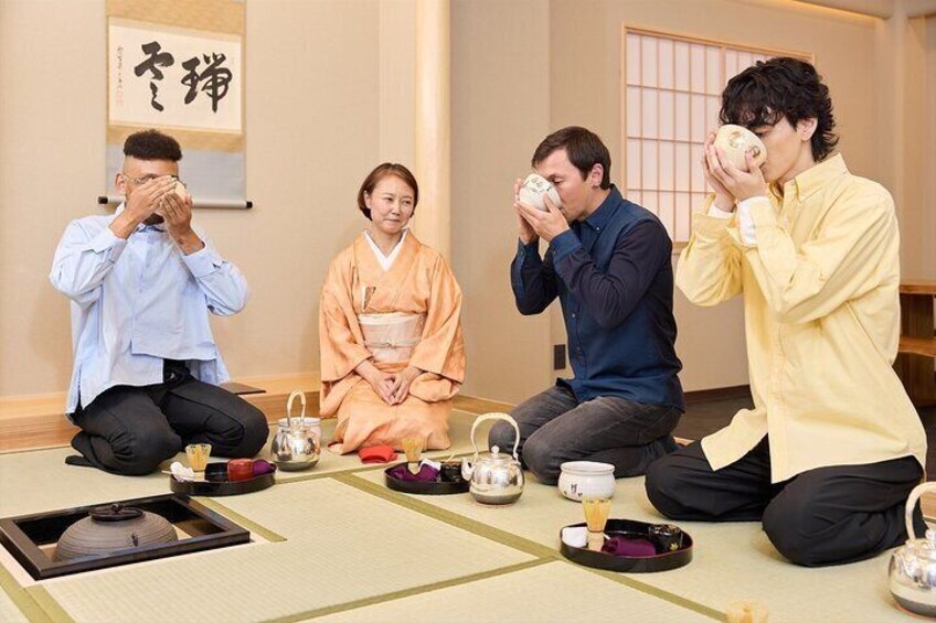 Four people sitting on tatami mats in a traditional Japanese room with tea sets. 1
