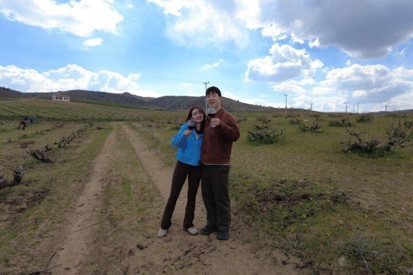 Two people standing on a dirt path in a grassy field with a hilly landscape in the background. 2