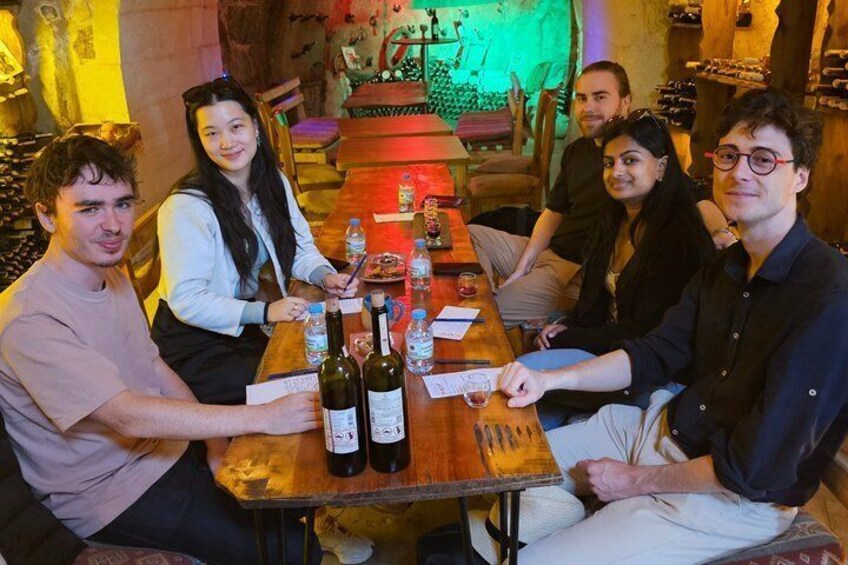 A group of people seated around a wooden table with bottles and papers, in a dimly lit room with a greenish hue. 5