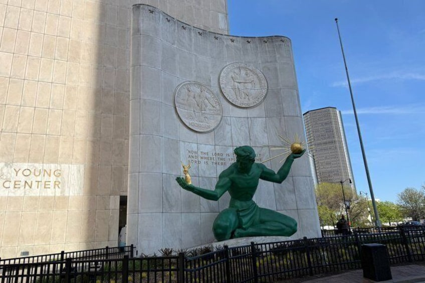A statue of a figure holding a scepter and a globe, with a plaque and two circular emblems on a building. 3