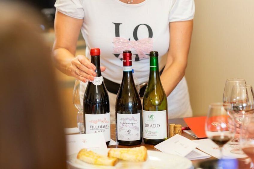 A woman standing behind a table with three wine bottles and glasses. 2