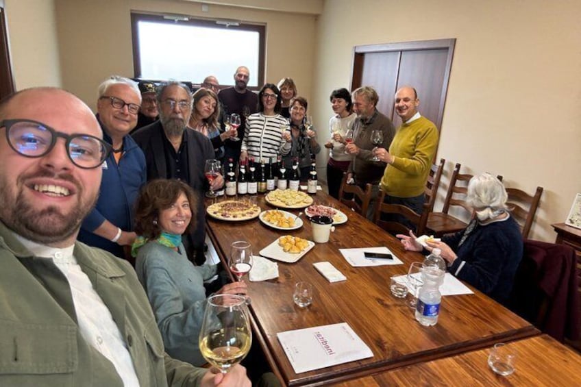 A group of people seated around a wooden table with plates of food and bottles of wine. 1