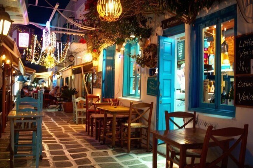 A narrow street with outdoor seating, blue shutters, and hanging lights. 2