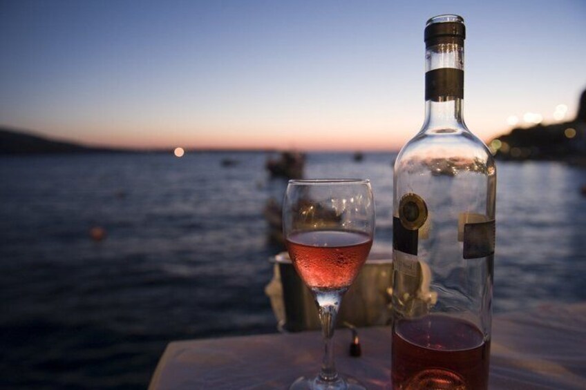 A bottle of red wine and a glass on a table by the sea at sunset. 3