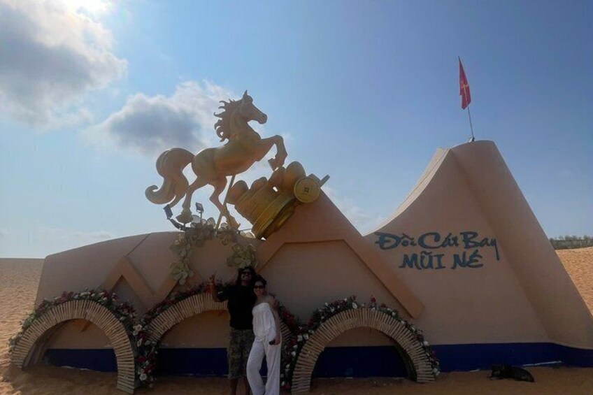 A large, beige monument with a horse figure, a flag, and the inscription 'Đại Cự Bay Mùi Nè'. 1