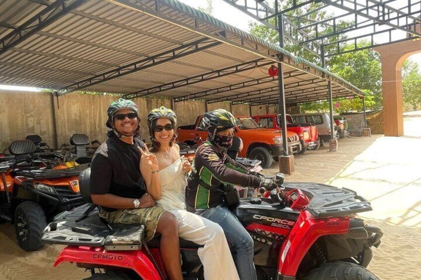 Three people on ATVs, a covered structure, and a red vehicle in the background. 3