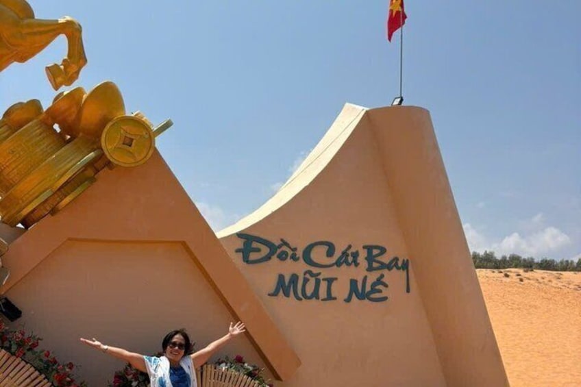 A large golden statue with a flag on top, a person with arms raised, and a wall with text. 2