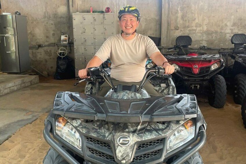 A person sitting on an ATV in a garage with other ATVs and a storage cabinet in the background. 5