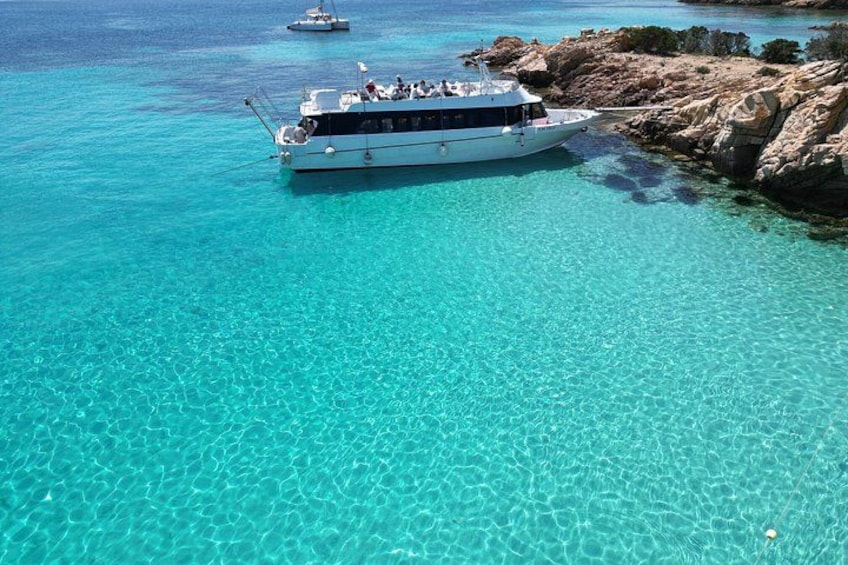 A boat anchored near rocky coastline with clear turquoise water. 2