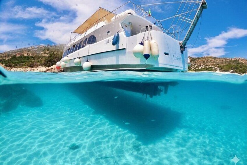 A white yacht named 'LM 1' anchored in clear turquoise waters with a rocky landscape in the background. 5