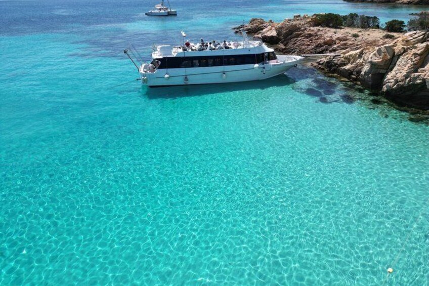 A boat anchored near a rocky coastline with clear turquoise water. 3