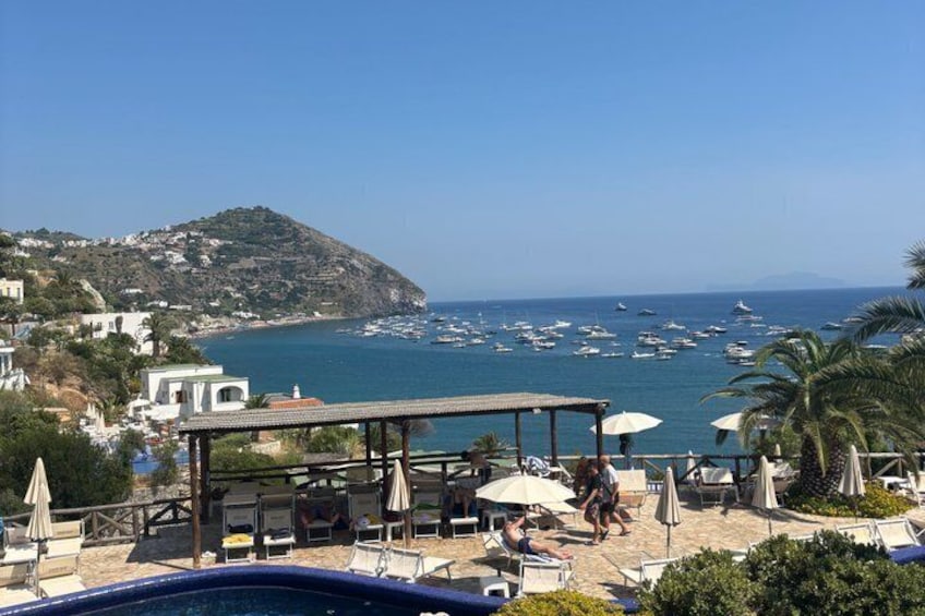 A coastal resort with a pool, umbrellas, and a view of boats on the sea. 1